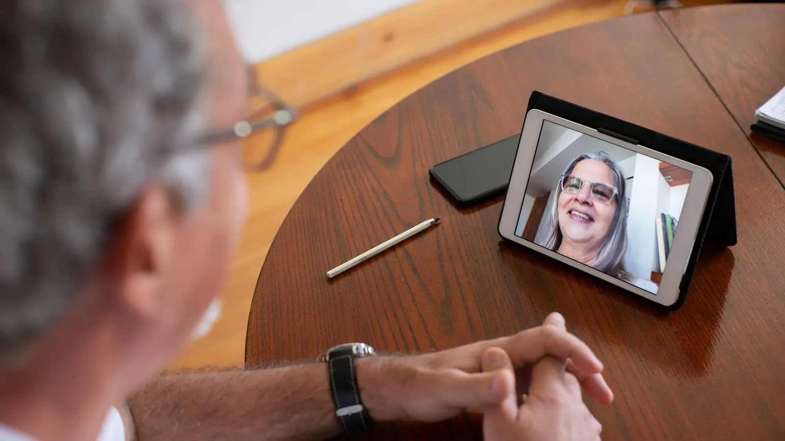 Senior man having a video call with a woman using a tablet at home, showcasing remote communication.