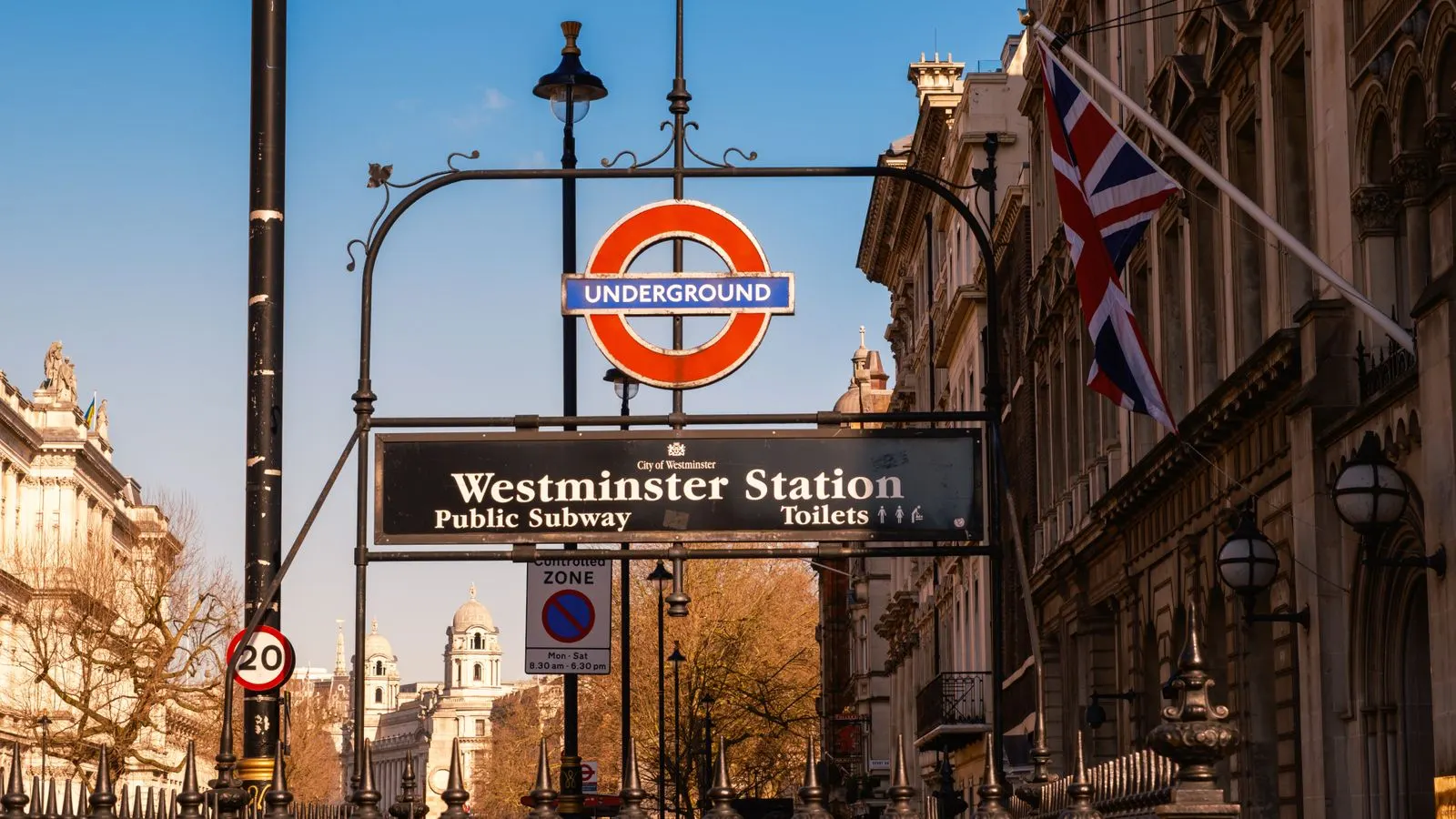 The Westminster Underground station sign with a Union flag and London buildings behind