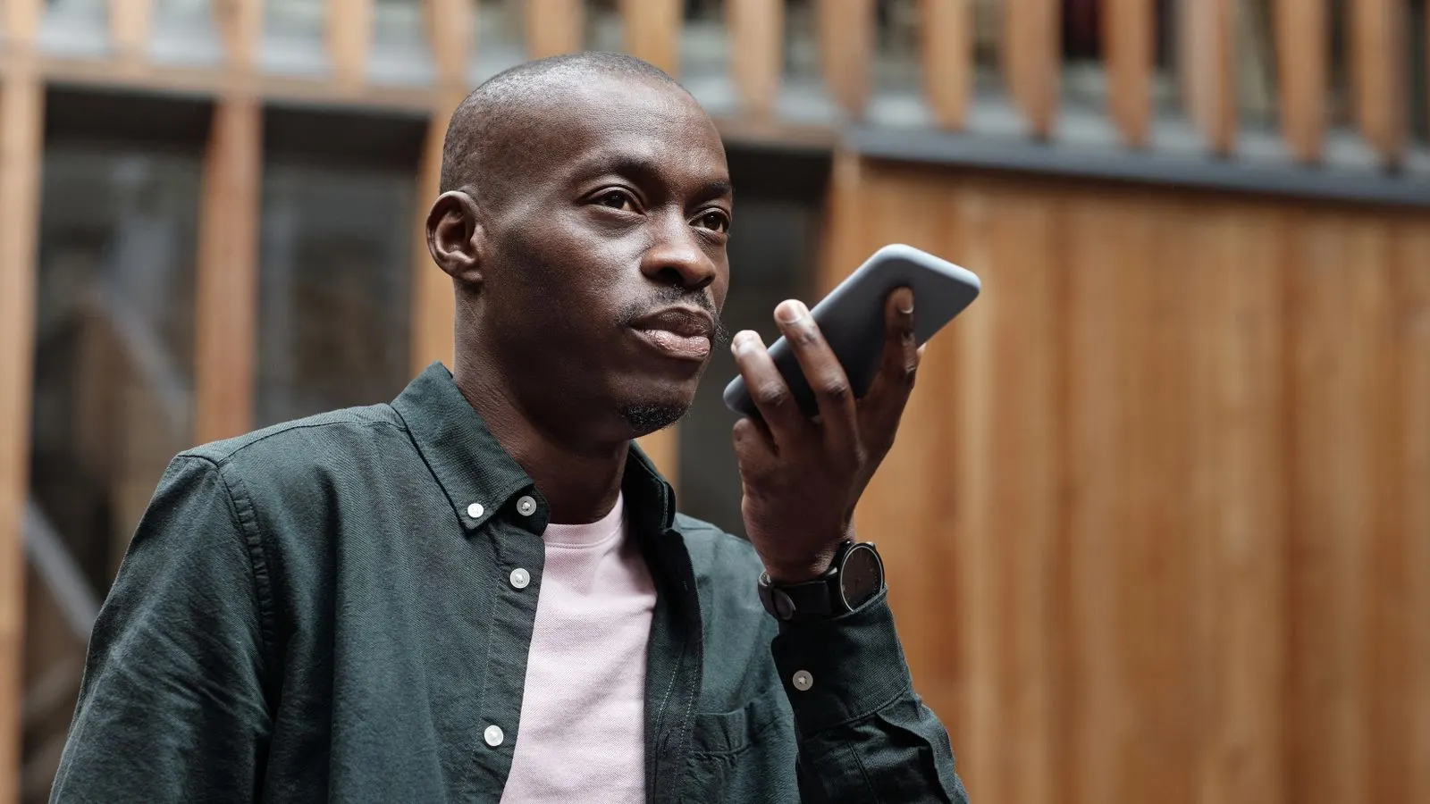 Stylish adult man using his smartphone for voice commands in an outdoor urban setting.