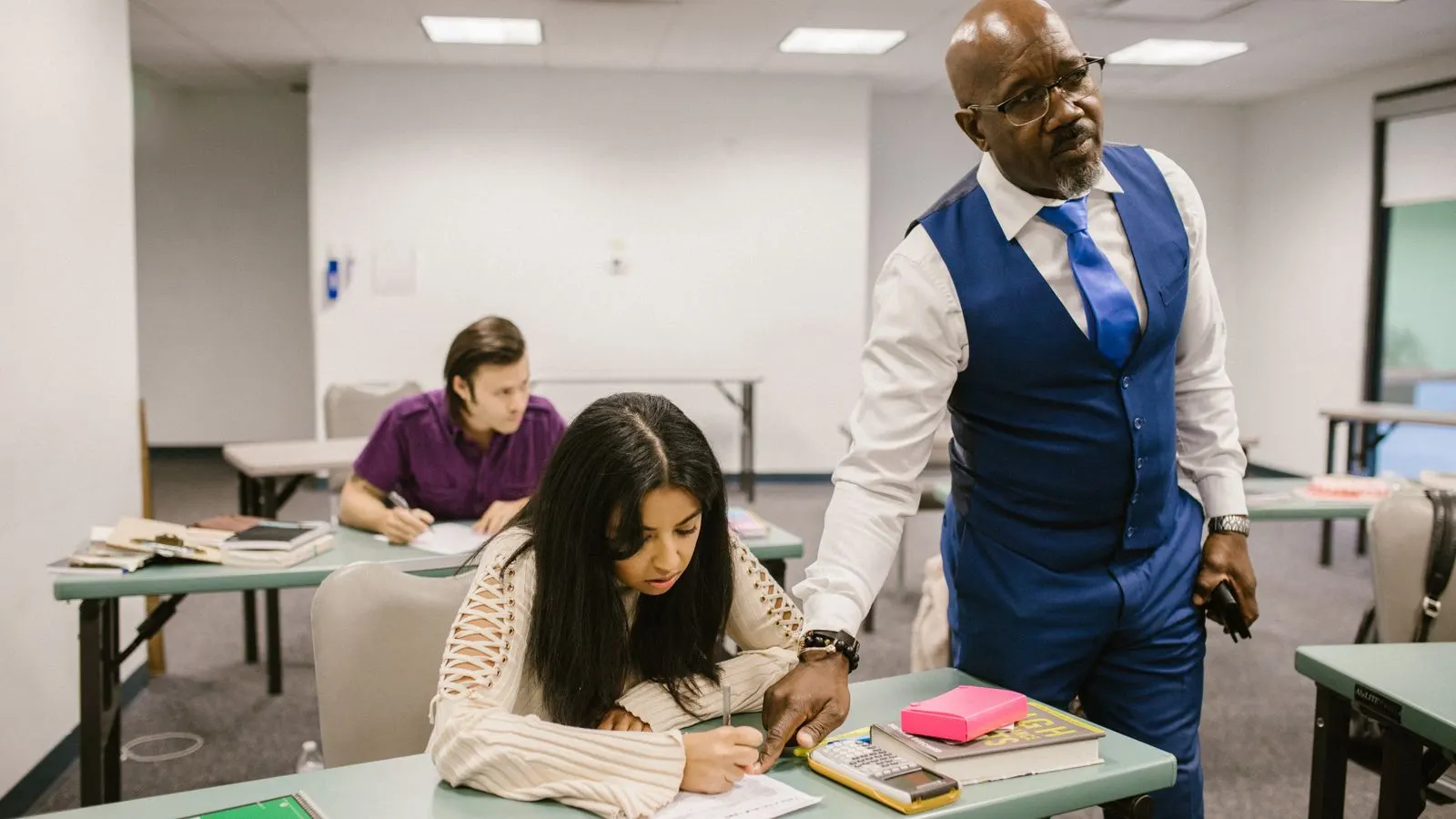 A teacher walking between desks while students write in a classroom