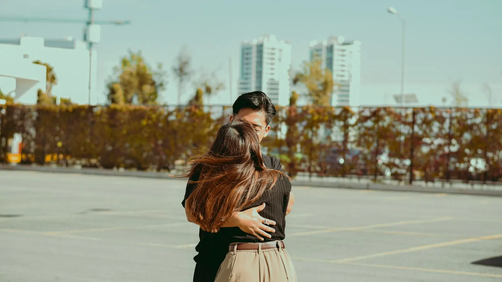 A warm embrace between a couple in a city parking lot with high-rise buildings.