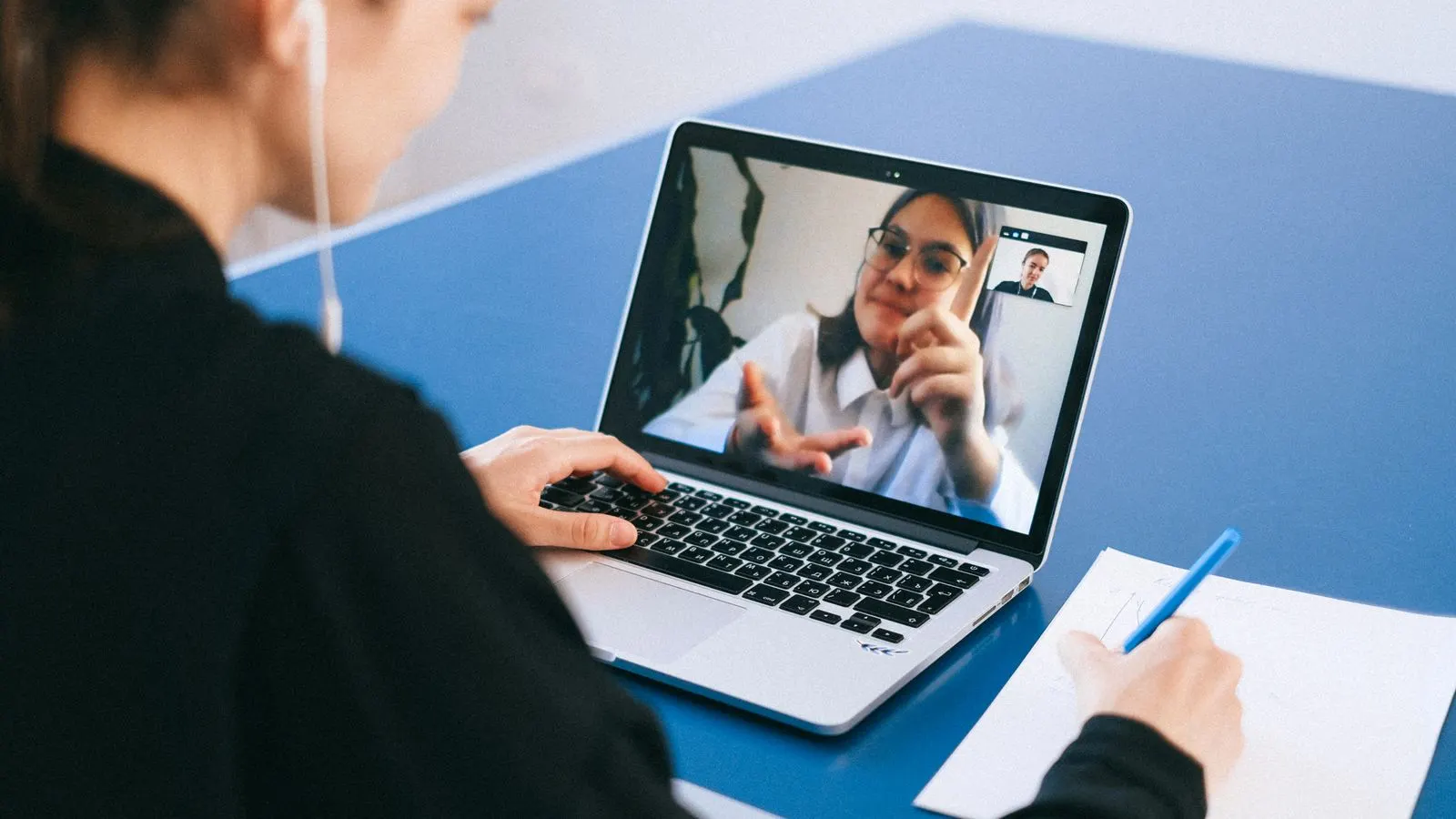 Woman participating in a virtual meeting, taking notes during a video conference on a laptop.